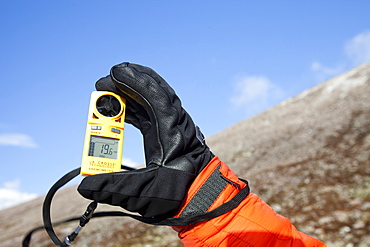 A mountaineer using an anemometer to measure wind speed and wind chill, in the Cairngorm mountains, Scotland, United Kingdom, Europe