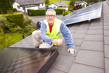 A workman fitting solar thermal panels for heating water, to a house roof in Ambleside, Cumbria, England, United Kingdom, Europe