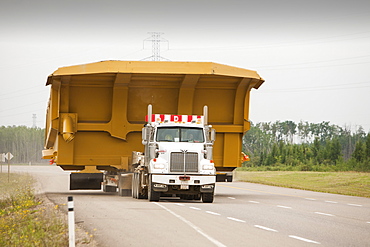 Truck hauls an oversize load, a massive dump truck used in the tar sands mines, on the road towards Fort McMurray, the centre of the tar sands industry, Alberta, Canada, North America