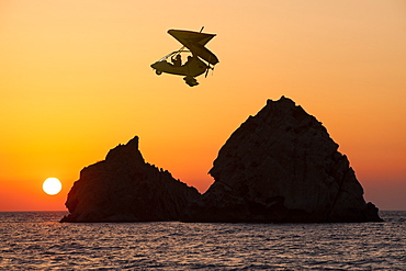 Motorised hang glider at sunset over rocky islands off Myrina on Lemnos, Greek Islands, Greece, Europe