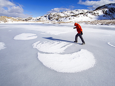 A climber on Sprinkling Tarn at the head of Borrowdale, looking towards Glaramara, with drifted snow making patterns on the ice, Lake District, Cumbria, England, United Kingdom, Europe