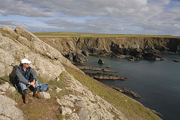 Man sitting on clifftop, looking out to sea, Deer Park, Martins Haven, Pembrokeshire, Wales, UK, Europe