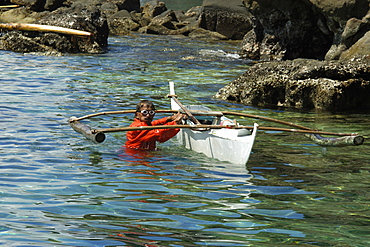 Fisherman wearing orange jumpsuit cleans his bangka (traditional Philippino boat), Apo Island, Negros, Philippines, Southeast Asia, Asia