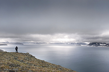 Whalebone Alley grand vista, female tourist standing on cliff face, Itygran Island (Bering Sea) Russia, Asia.  MORE INFO: Whale Bone Alley was discovered by Soviet archaeologists in 1976, but has remained untouched since and little is known of this place. There is a long double line of bowhead whale bones -- jaws and ribs -- running parallel along the shore for hundreds of yards. Many of the bones, especially the enormous jaw bones, are still standing, propped up by lichen-covered rocks. The location is thought to have been used in about 1300 as a ceremonial site, for a men's secret society or feasting site.