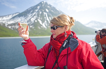 Views from the Clipper Odyssey towards Russkaya Bay of volcanic mountains in mist and sun set, Woman with champagne, Russkaya Bay (Bering Sea), Russia, Asia.