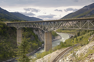 A truss road bridge crossing a Glacial river in the Alaskan Interior, Denali, spanning both the valley and a rail track.  Mountainous landscape in background. Denali, Alaska, USA