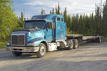 Blue Eagle, American Tractor with trailer attached.  Parked up in a layby next to a forest.  Sunny in the Alaskan Interior. The Interior, Alaska, USA