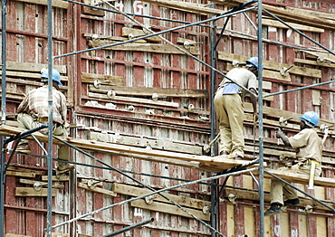 Three construction workers, all with safety hats work rather precariously on the meagre scaffolding, on a construction site in downtown Kigali, Rwanda. Kigali, Rwanda, East Africa