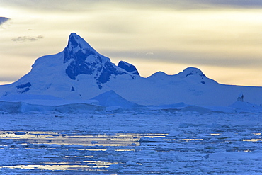 Sunset on snow capped mountains and icebergs surrounded in brash ice in Crystal Sound near the Antarctic Circle on the west side of the Antarctic Peninsula.