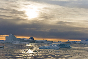 Sunset on snow capped mountains and icebergs surrounded in brash ice in Crystal Sound near the Antarctic Circle on the west side of the Antarctic Peninsula.