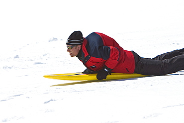 Lindblad Expeditions guests riding a snow board down a hill in Antarctica as part of expedition travel. NO MODEL RELEASES FOR THIS IMAGE.