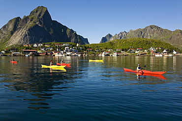 Kayakers in the late evening light on the picturesque Norwegian fishing town of Reine in the Lofoton Island Group, Norway. No model or property releases.