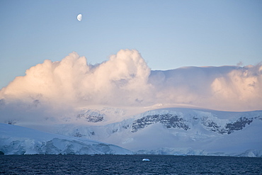 The Lindblad Expedition ship National Geographic Explorer in Dahlman Bay in late evening light as the waxing moon rises on the west side of the Antarctic Peninsula in Antarctica. 