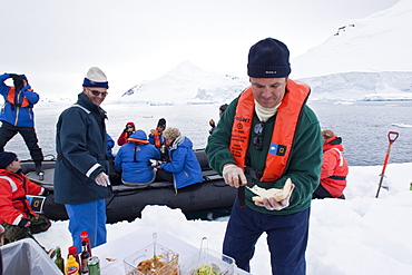 Guests from the Lindblad Expedition ship National Geographic Explorer enjoy a hot asado sandwich prepared by staff at BBQ on an ice floe near Adelaide Island, Antarctica