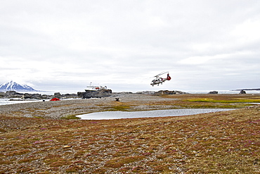 Helicopter bringing supplies to repair the hunters cabin at Gnalodden cliff in Hornsund, Norway