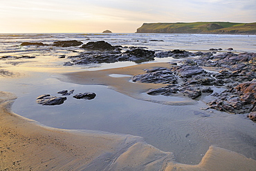 Tide retreating at sunset leaving tide pools among rocks, with Pentire Head in the background, Polzeath, Cornwall, England, United Kingdom, Europe