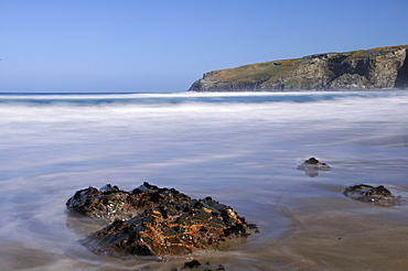 A rising tide swirls around a rock on the beach at Trebarwith Strand, Cornwall, England, United Kingdom, Europe