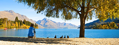 Panorama of a tourist relaxing by Lake Wakatipu in autumn at Queenstown, Otago, South Island, New Zealand, Pacific