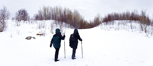 Tourists hiking by frozen lake in the Arctic Circle on Ringvassoya Island in the region of Tromso, Northern Norway