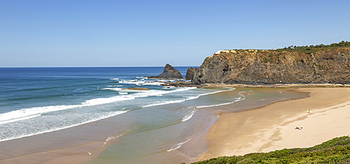 Coastline view of headlands and bay with wide sandy beach, surfer and a few sunbathers, Praia de Odeceixe, Algarve, Portugal, Europe