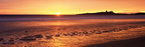 Dunstanburgh castle at sunrise, view across Embleton Bay, Northumberland, England, United Kingdom, Europe