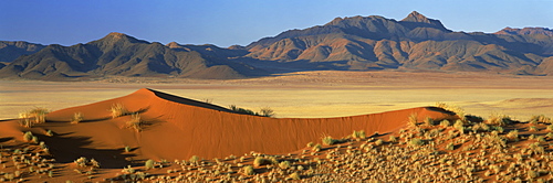 Panoramic view over orange sand dunes towards mountains, Namib Rand private game reserve, Namibia, Africa