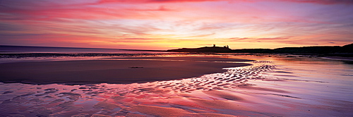 Embleton Bay at sunrise, low tide, with Dunstanburgh Castle in distance, Northumberland, England, United Kingdom, Europe