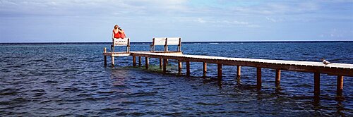 Rear view of mother and her daughter sitting on a bench at a pier, Belize