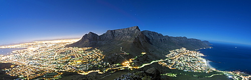 Panoramic view of Table Mountain and the city of Cape Town in moonlight. Table Bay can be seen far left and the Atlantic Ocean coastline and suburb of Camps Bay and its beach can be seen far right.