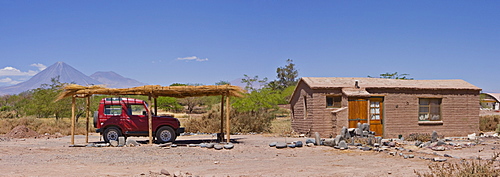 Four-wheel drive vehicle parked under sun shade in front of a small clay house, Licancabur Volcano in background, San Pedro de Atacama, Chile, South America