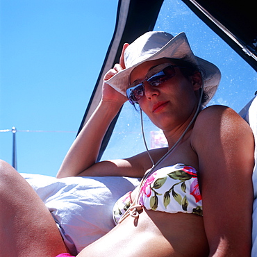 Woman wearing bikini, sunglasses and a hat sitting on sailboat and looking at camera, Dalmatia, Croatia