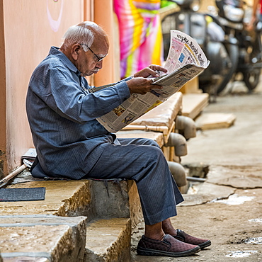 A senior man sits on the side of a street reading the newspaper, Jaisalmer, Rajasthan, India