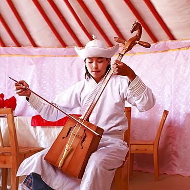 Young man in traditional dress plays horse head fiddle in a ger, Gobi Desert, Mongolia, Central Asia