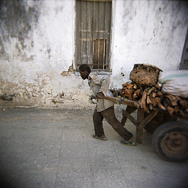 Man pulling cart along narrow street, Stone Town, Zanzibar, Tanzania, East Africa, Africa