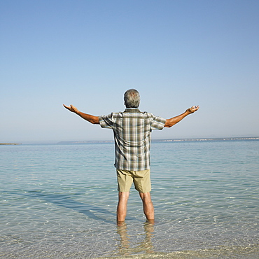 Happy senior man on beach with arms raised