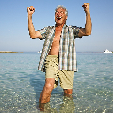 Happy senior man on beach with arms raised
