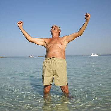 Happy senior man on beach with arms raised
