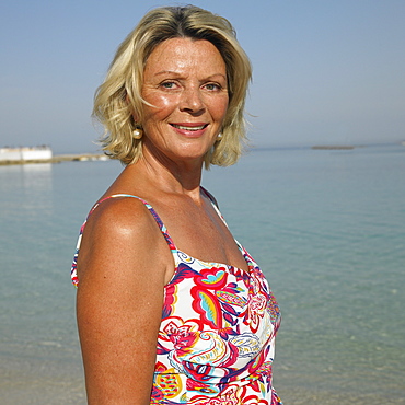 Senior woman on beach with arms raised