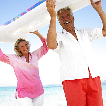 senior couple on beach holding air bed