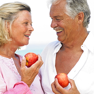 senior couple on beach holding apples