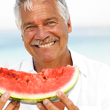 Senior man on beach holding water melon
