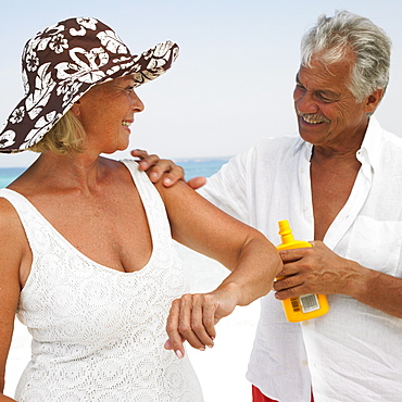 Senior couple on beach, man applying suncream to woman