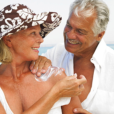 Senior couple on beach, man applying suncream to woman