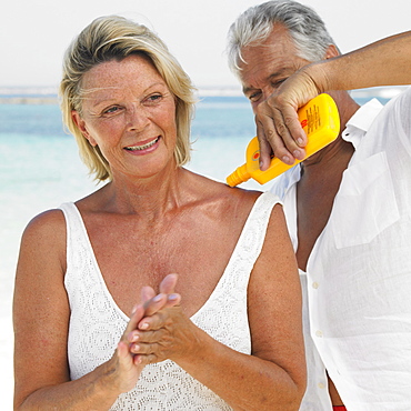 Senior couple on beach, man applying suncream to woman