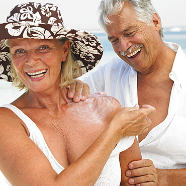 Senior couple on beach, man applying suncream to woman