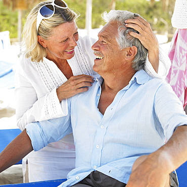 senior couple on beach on sunloungers