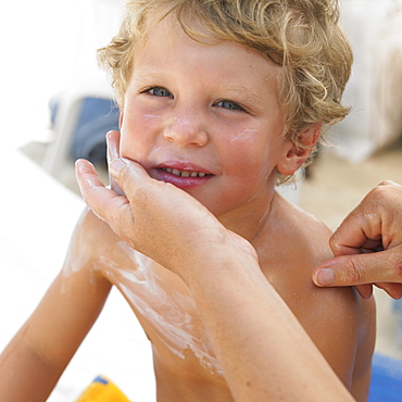 Boy (6-8) on beach having suncream applied