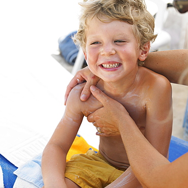 Boy (6-8) on beach having suncream applied
