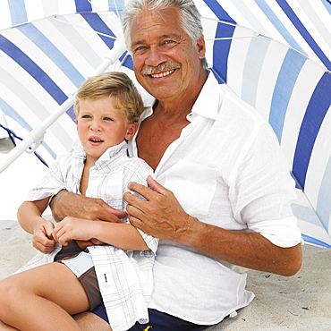 Grandfather and grandson (6-8) on beach under parasol