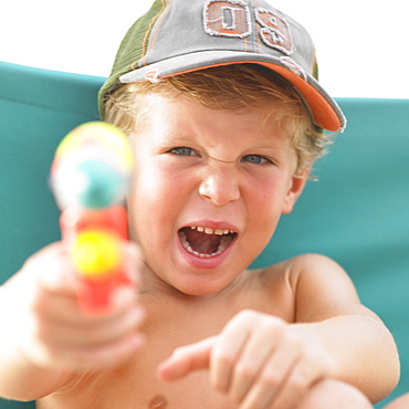 Boy (6-8) on sunlounger holding water pistol